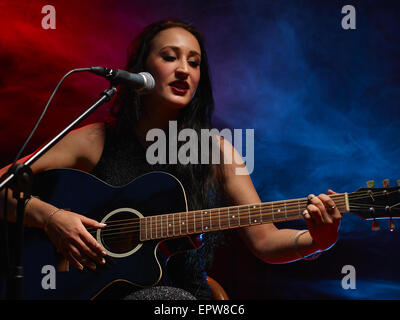 Beautiful woman plays a guitar, smoky stage on background Stock Photo