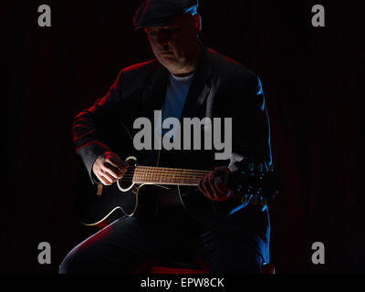 Mature man plays a guitar, smoky stage on background Stock Photo