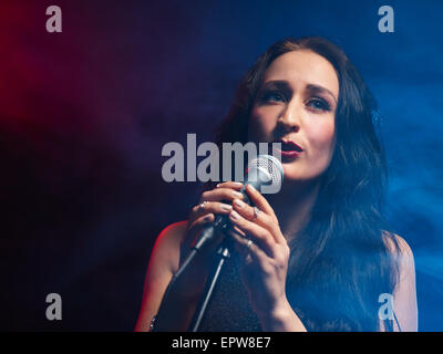 Beautiful woman sings, smoky stage on background Stock Photo