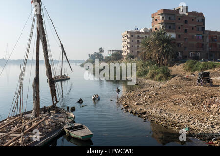 Calesh drivers bathe their horses in the Nile at Edfu in front of a large felucca carrying stone for construction Stock Photo