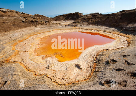 Sinkhole or open pit with orange salty water on the shore's of the dead sea at the end of the summer when the water level is at