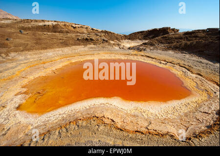 Sinkhole or open pit with orange salty water on the shore's of the dead sea at the end of the summer when the water level is at