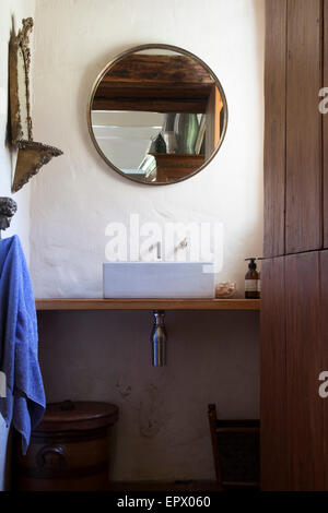 Guest bathroom sink set on wooden vanity with round mirror reflecting wooden ceiling and hanging purple towel in South African home Stock Photo