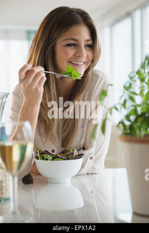 Young woman eating salad in living room Stock Photo