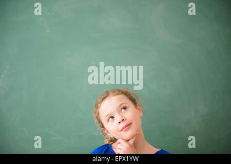 Girl (10-11) thinking in front of green blackboard Stock Photo