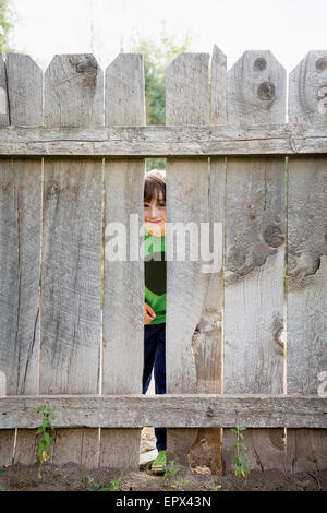 Boy (6-7) looking through hole in fence Stock Photo