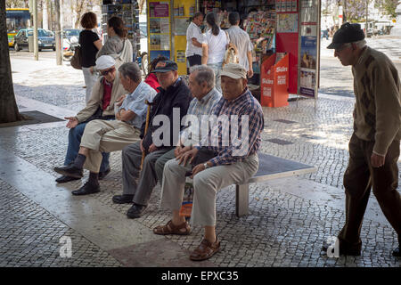 Group of mature local portuguese men sitting on a bench in the street chatting Stock Photo