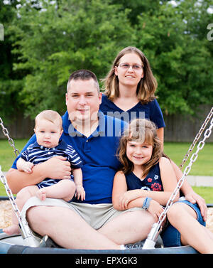 Family posing on a swing at an outdoor park playground Stock Photo