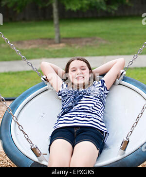Teenage girl swings on a saucer swing at a park playground Stock Photo