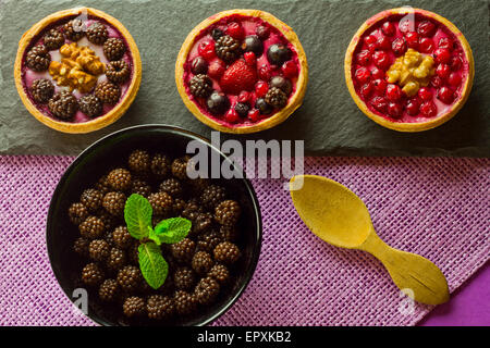 Three autumn fruits cakes on a slate plate and a bowl of blackberries on purple background Stock Photo