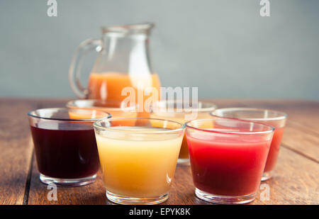 six glasses of variety of organic juices with a jug of juice in the background on a wooden vintage table Stock Photo