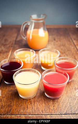 six glasses of variety of organic juices with a jug of juice in the background, on a wooden table Stock Photo