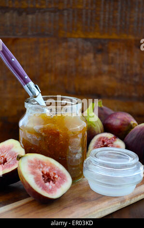 Fresh figs on wooden cutting chopping board with jar of fig jelly preserve on dark wood rustic table background. Stock Photo