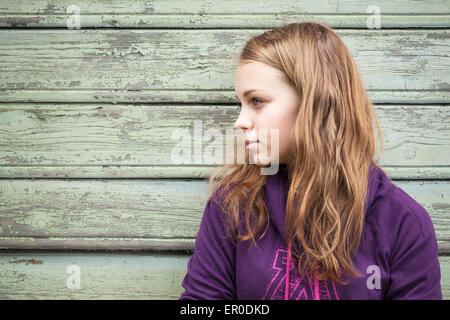 Beautiful blond Caucasian girl  teenager, closeup profile outdoor portrait over green wooden wall Stock Photo