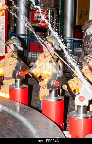 Children's activity centre, Kidzania in Nishinomiya, Japan. Interior. A row of children dressed as firemen manning hoses directing water upwards. Stock Photo