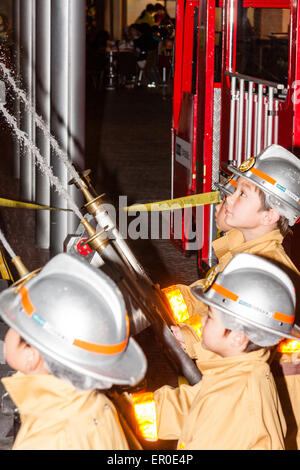 Children's activity centre, Kidzania in Nishinomiya, Japan. Interior. A row of children dressed as firemen manning hoses directing water upwards. Stock Photo