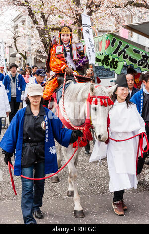 Young woman dressed in Heian period costume of a samurai warrior with a mae-tengan head dress, on white horse at the Genji parade at Tada, Japan. Stock Photo