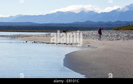 Walker at the seaward entrance to the Okarito Lagoon looking towards the Southern Alps In New Zealand South Island Stock Photo