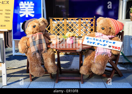 Two stuffed teddy bears wearing scarfs and woolly hat arranged sitting at table, drinking tea on the pavement outside a cafe in Hamamatsu, Japan. Stock Photo