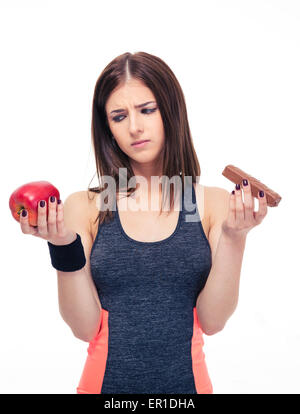 Sports woman making choice between healthy apple and unhealthy chocolate isolated on a white background. Stock Photo