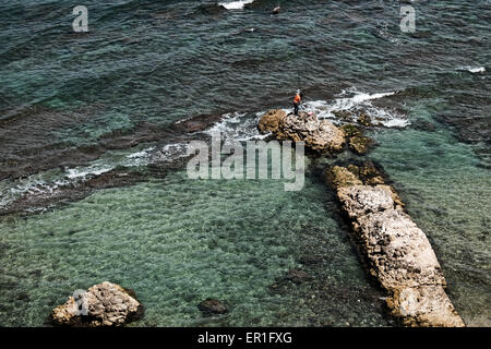 Apollonia National Park, Israel. 24th May, 2015. A fisherman stands on the stone remains of an ancient dock bellow the Crusader Fortress Arsouf. Apollonia National Park, named after the god Apollo, is located on a cliff named Tel Arshaf overlooking the Mediterranean, north of Tel-Aviv. Founded by the Phoenicians in the Persian Period (6th century BCE) it was conquered from the Muslims by the Crusaders in 1191 CE. The fortress was built in 1241 CE dominating the harbor. The Crusader city was walled and surrounded by a moat. Credit:  Nir Alon/Alamy Live News Stock Photo