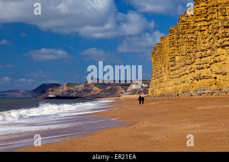 Walkers on the beach below the distinctive banded sandstone strata of East Cliff on the Jurassic Coast, Dorset, England, UK