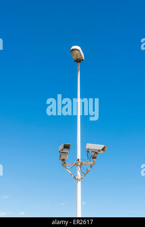 Two security cameras attached to a lamppost against blue sky Stock Photo