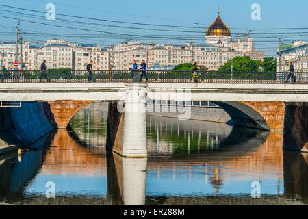 Moscow, Russia. 25th May, 2015. Beginning of the business week in Moscow, Russia. Monday, May 25, 2015. Unidentified people cross the Iron Bridge over the bypass canal of the Moscow river on their way to work. You can see green trees of the Bolotnaya (marshy) square and the golden dome of the Cathedral of Christ the Savior in the background. In the background you can also see the famous House on embankment. Illustrative editorial use only. Credit:  Alex's Pictures/Alamy Live News Stock Photo