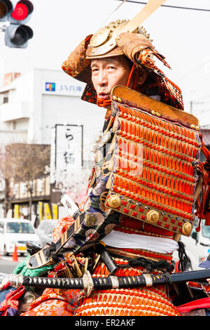 Japanese man dressed in full samurai armour and Kabuto helmet, on horseback riding through city street in the Genji parade at Tada in Japan. Stock Photo