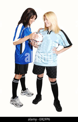 Two young pretty soccer woman, holding a soccer ball and wearing the uniform of there club, standing in the studio for light gra Stock Photo