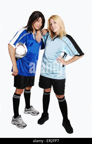 Two young pretty soccer woman, holding a soccer ball and wearing the uniform of there club, standing in the studio for light Stock Photo