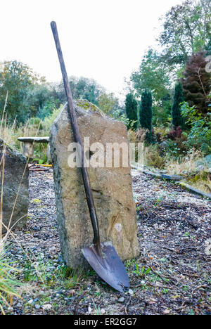 Grave digger's long handled shovel leaning up against a gravestone at a grave yard. Stock Photo