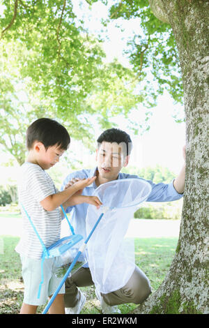 Happy Japanese father and son catching insects in a city park Stock Photo