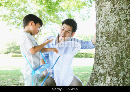 Happy Japanese father and son catching insects in a city park Stock Photo