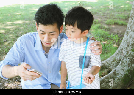 Happy Japanese father and son catching insects in a city park Stock Photo