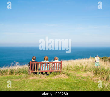 People sitting on bench overlooking sea on cliffs at Kettleness on the North Yorkshire coast near Whitby, England, UK Stock Photo