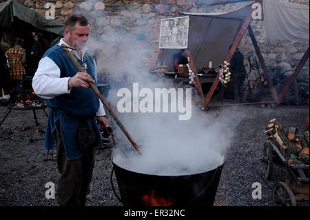 Man in traditional medieval outfit stirs soup in large cauldron pot over open fire during a medieval crafts event in Trakai Island Castle ( Lithuanian: Traku salos pilis ) located on an island in Lake Galve in Lithuania Stock Photo