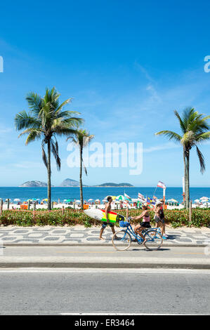 RIO DE JANEIRO, BRAZIL - MARCH 08, 2015: Brazilians walk and ride bicycles with surfboards on the beachfront boardwalk Ipanema. Stock Photo