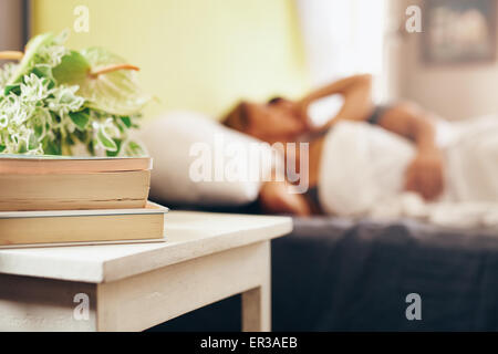Side table with books and flowers by the bed in bedroom. Couple sleeping peacefully on bed.