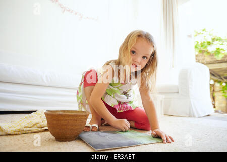 Portrait of innocent little girl painting a picture. Schoolgirl sitting on the floor coloring looking at camera smiling. Stock Photo