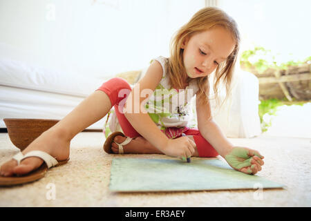 Shot of cute little baby girl coloring picture while sitting on floor at home. Stock Photo