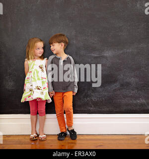 Little boy and girl standing in front of blackboard looking at each other. Indoors shot of children at home with copy space. Stock Photo