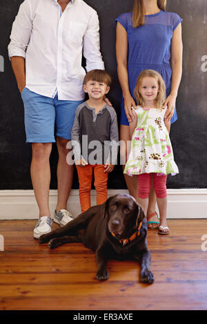 Cropped shot of lovely young family with their pet dog. Labrador retriever sitting on floor with kids and their parents standing Stock Photo