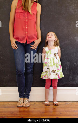 Cropped shot of woman with her daughter. Little girl looking at her mother standing by a black wall at home. Stock Photo