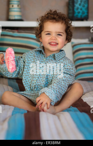 Smiling girl sitting on a bed reading a book Stock Photo - Alamy