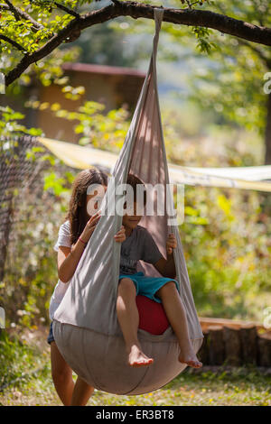 Girl pushing a boy on a swing in the garden Stock Photo