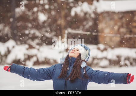 Girl standing in the snow looking up at the sky with outstretched arms Stock Photo