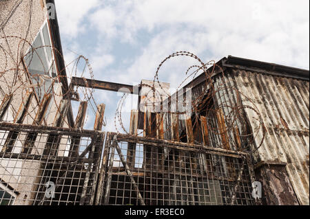 old metal steel gate in run down buildings protected with corrugated metal and sharp razor wire fence as keep out Stock Photo