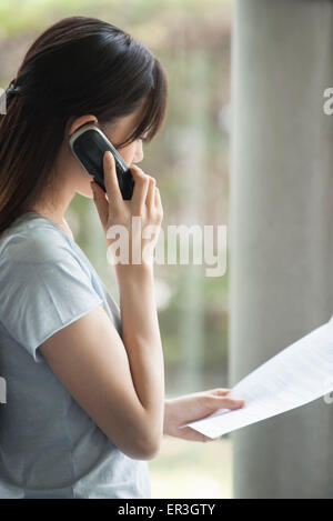 Woman talking on cell phone, looking at document Stock Photo