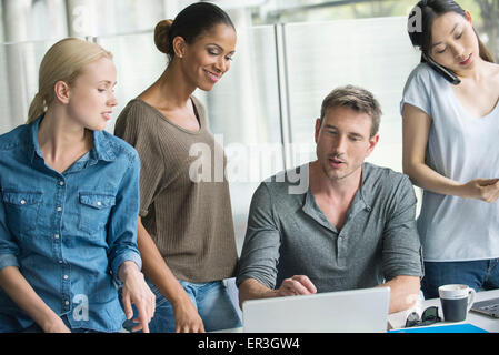 Workers gathered around desk of colleague Stock Photo